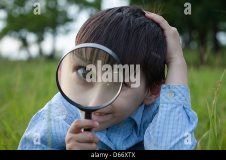 Ragazzo con lente di ingrandimento sdraiati sull'erba Foto Stock