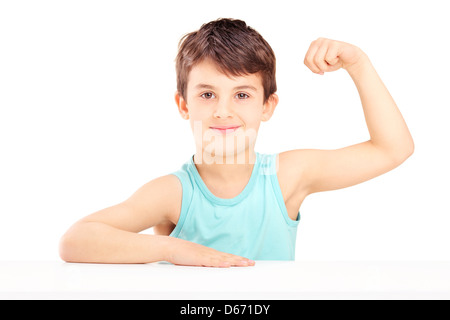 Un bambino che mostra i suoi muscoli seduto su un tavolo isolato su sfondo bianco Foto Stock