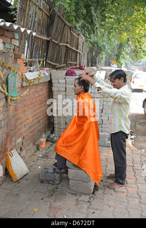 Un barbiere che dà al suo cliente un massaggio della testa su un marciapiede di strada in Janpath Lane, Nuova Delhi, India. Foto Stock