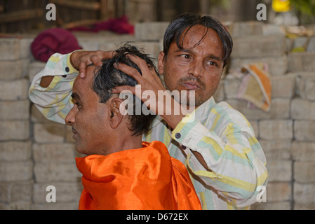Un barbiere che dà al suo cliente un massaggio della testa su un marciapiede di strada in Janpath Lane, Nuova Delhi, India. Foto Stock