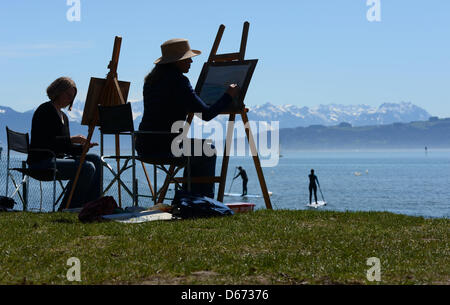 Zwei Frauen malen am 14.04.2013 in Wasserburg (Bayern) am Bodensee, während im Hintergrund Wassersportler zu sehen sind. Die Teilnehmer eines Malkurses aus Lindenberg malen die Kirche von Wasserburg. Foto: Felix Kästle/dpa +++(c) dpa - Bildfunk+++ Foto Stock