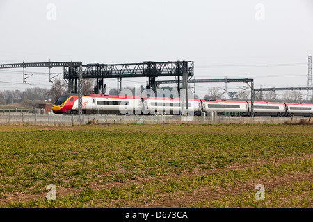 Una vergine treno passa sotto un gantry segnali sulla costa ovest Mainline. Foto Stock