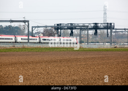 Una vergine treno passa sotto un gantry segnali sulla costa ovest Mainline. Foto Stock