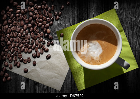 Tazza di cappuccino, caffè vecchio foglio di carta verde, igienico e fagioli su tavoli in legno nero, vista dall'alto Foto Stock