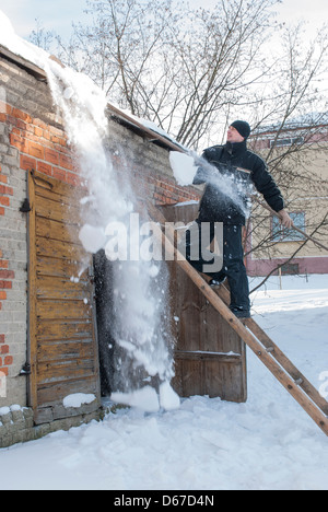 L'uomo la rimozione di neve pesante dal tetto di un edificio Foto Stock