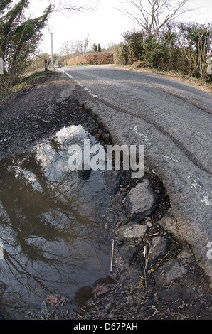 Buche in strada di campagna causato da neve e gelo runoff di fusione crea un pericolo di pericolose per i ciclisti automobilista Foto Stock