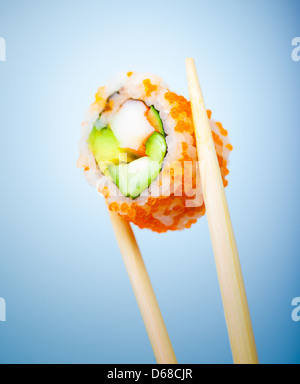 Gustoso rotolo di sushi con polpa di granchio, cetriolo, avocado e caviale rosso in bacchette isolato su sfondo blu, il cibo giapponese Foto Stock