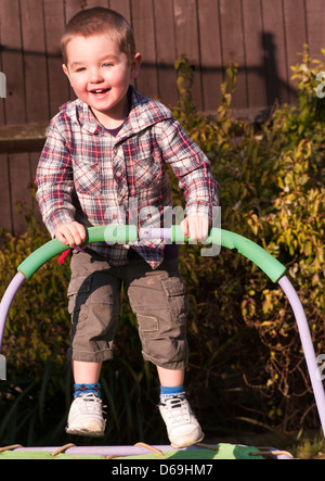 3 anno vecchio ragazzo con capelli corti rimbalza su un trampolino da giardino Foto Stock