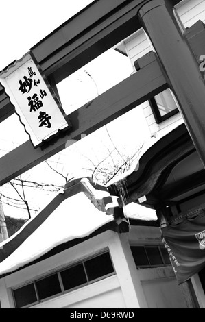 Una porta torii ad Hakodate, Hokkaido, Giappone, circondata dalla neve in inverno, che cattura l'elemento architettonico tradizionale giapponese in mezzo a un paesaggio innevato. Foto Stock
