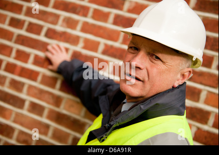 Edificio ingegnere controllo della muratura di un edificio. L'uomo guarda la fotocamera e indossa il suo bianco casco di sicurezza. Foto Stock