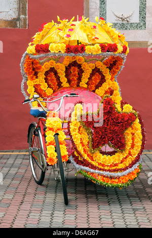 Uno dei tanti risciò triciclo per gite turistiche decorate con luminosi colorati fiori di seta in Melaka Malaysia Foto Stock