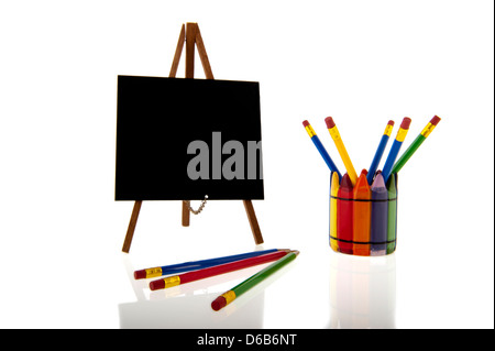 Una lavagna su cavalletto treppiedi accanto a un collage di colorfull matite in una tazza isolata su uno sfondo bianco Foto Stock