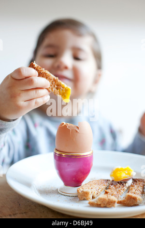 Ragazza dipping toast con le uova a colazione Foto Stock