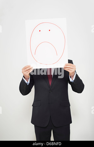 Imprenditore tenendo una faccina triste sul suo volto Foto Stock