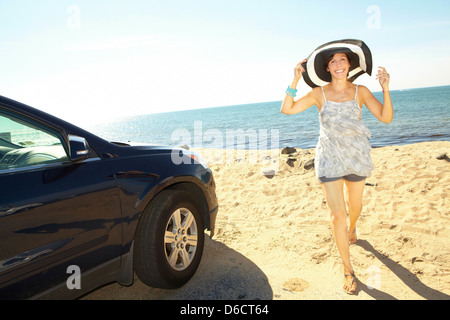 Donna con grande spiaggia hat camminare sulla sabbia dall' oceano accanto a AUTO nera Foto Stock