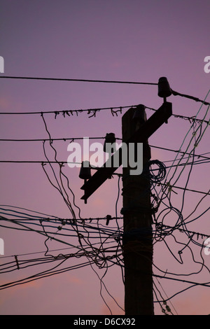 Silhouette di un palo elettrico mal mantenuto a Chennai, India durante il tramonto, con un cielo viola Foto Stock