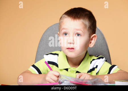 Little Boy Disegno con matite di colore su sfondo arancione Foto Stock