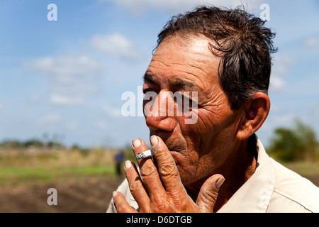 Ritratto di uomo cubano che fuma sigaretta mentre è al lavoro come agricoltore in campo agricolo. Contadino ispanico che lavora alla cooperativa agraria ANAP a Guines, Cuba Foto Stock