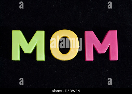 Mom scritto con il giocattolo per bambini è colorato le lettere magnetiche isolate su uno sfondo nero Foto Stock