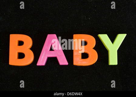 Baby scritto con il giocattolo per bambini è colorato le lettere magnetiche isolate su uno sfondo nero Foto Stock