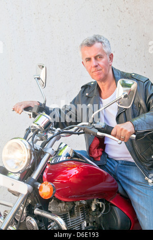 Ritratto di un Caucasian di motociclisti in un abbigliamento sportivo a labbro di tenuta cercando in lente seduto su un incrociatore rosso. Generico posizione shot Foto Stock