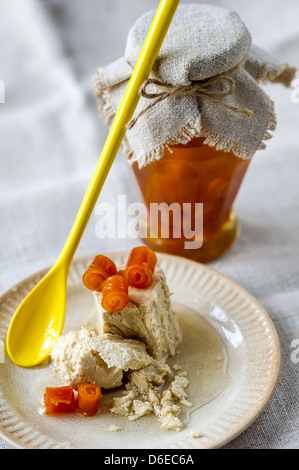Vaso di vetro di marmellata di arancio, giallo cucchiaio e dolce halva ritorto con bucce di arancia su una piastra Foto Stock