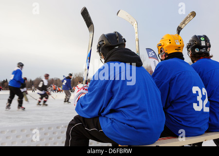 I giocatori guarda l'azione dal banco di squadra durante una partita presso l'U.S. Pond Hockey campionati sul lago Nokomis. Foto Stock