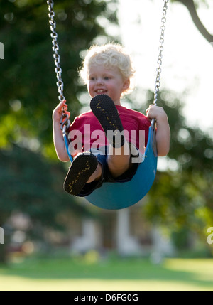 Capelli biondi boy basculante in una swing sul parco giochi. Foto Stock