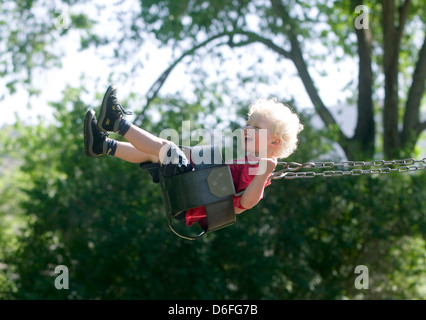 Capelli biondi boy basculante in una swing sul parco giochi. Foto Stock