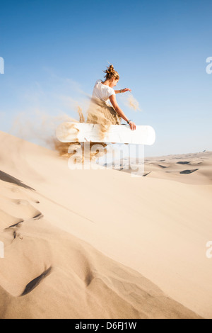 Giovane donna sandboarder jumping e tenendo premuto il suo bordo sul deserto che circonda Huacachina Oasis, nel sud-ovest del Perù. Foto Stock