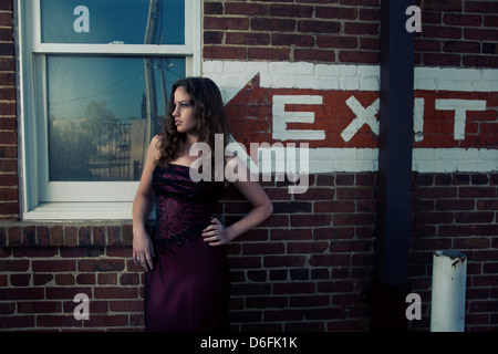 Donna in piedi contro un muro di mattoni accanto alla finestra Foto Stock