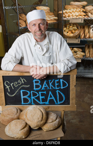 Ritratto di cuoco professionista nel suo panificio, circondato da pane fresco Foto Stock