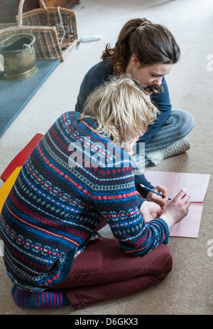 Ragazzo adolescente e la ragazza seduta su un soggiorno moquette si aiuta a vicenda con una matematica GCSE pratica di carta e di revisione per gli esami Foto Stock