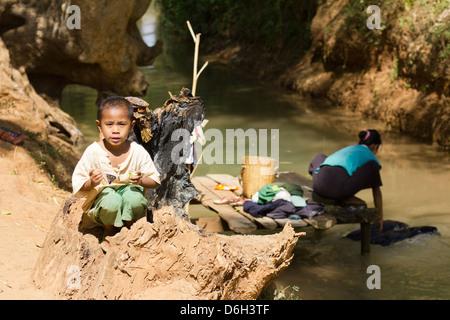 Giovane ragazzo da un flusso mentre sua madre fa il lavaggio - Inn Thein Village 1 Foto Stock