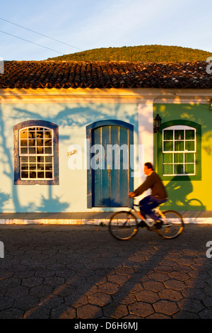 Uomo in sella ad una bicicletta nella parte anteriore di una casa coloniale nel centro storico di Ribeirao da Ilha. Foto Stock