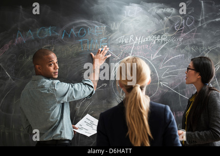 L'uomo scrivere sulla lavagna, i colleghi a guardare Foto Stock