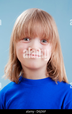 Ritratto in studio di un ragazzo con lunghi capelli biondi - isolato su blu Foto Stock