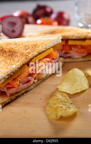 Ritratto closeup di toast al prosciutto e formaggio sandwich di pomodoro con croccantini su una breadboard di legno Foto Stock