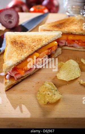 Toast al prosciutto e formaggio sandwich di pomodoro con croccantini su una breadboard di legno Foto Stock