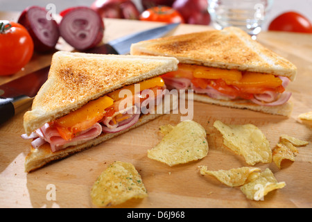 Toast al prosciutto e formaggio sandwich di pomodoro con croccantini su una breadboard di legno Foto Stock