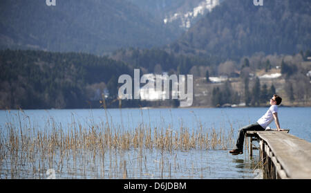 Illustrazione - un'immagine illustrata mostra un giovane uomo seduto su di un molo al Tegernsee, Germania, 15 marzo 2012. Sunshines e temperature fino a venti gradi centigradi sedotto tanti per andare all'esterno. Foto: Marc Mueller Foto Stock