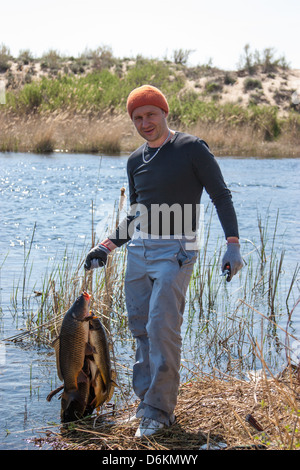 Felice Fortunato pescatore tenendo un grande carpa sul fiume. La mattina presto sulla pesca Foto Stock