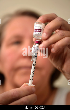 Una femmina senior prepara una siringa da insulina, che è usato per trattare il diabete. Foto Stock