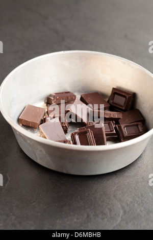 Primo piano della vasca di contenimento dei pezzi di cioccolato su sfondo scuro Foto Stock