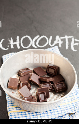 Recipiente contenente i quadrati di cioccolato con cioccolato di parola scritta in gesso su sfondo scuro Foto Stock