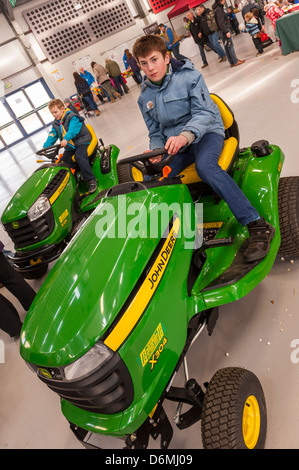 Un ragazzo di 13 anni seduto su un John Deere trattore di piccole dimensioni a molla si sollevano in Norwich , Norfolk , Inghilterra , Inghilterra , Regno Unito Foto Stock