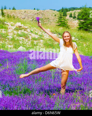 Felice donna bionda con bouquet floreali danza su viola campo di lavanda, avendo divertimento all'aperto, estate Concetto di vacanza Foto Stock