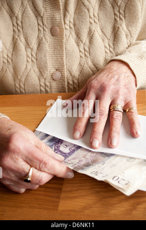 Donna anziana mettere venti pound note in una busta Foto Stock