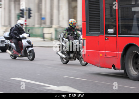 Due motociclisti in viaggio dietro un bus, lungo una strada a Londra, Inghilterra. Foto Stock