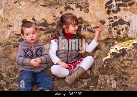 Giovane fratello e sorella vestito in abiti caldi seduti insieme all'esterno Foto Stock